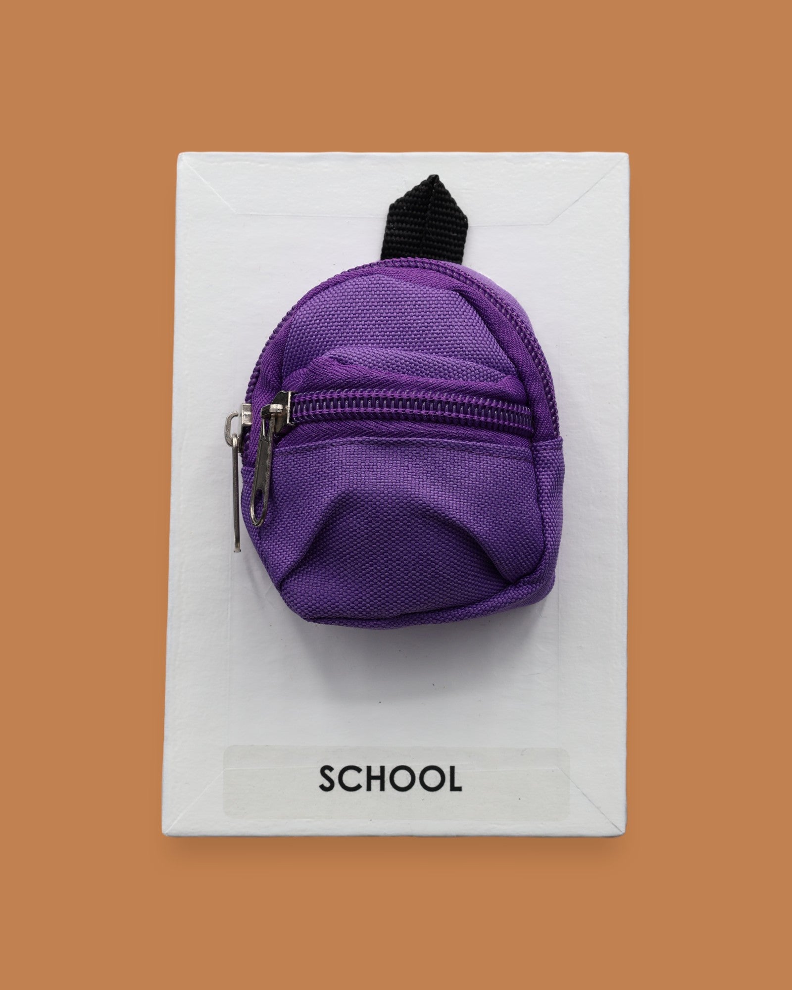 The School Backpack symbol with a colorful miniature backpack embedded in the center. Color of backpack may vary. Labeled "School" in black front on white backing at the bottom of the symbol. The background of the symbol is white. 