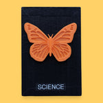 The Science symbol has a circular black magnet with a blue string attached to the magnet for security embedded in the center. Labeled "Science" in black font and white backing. The background of the symbol is white. 