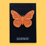 The Science symbol has a circular black magnet with a blue string attached to the magnet for security embedded in the center. Labeled "Science" in black font and white backing. The background of the symbol is white. 