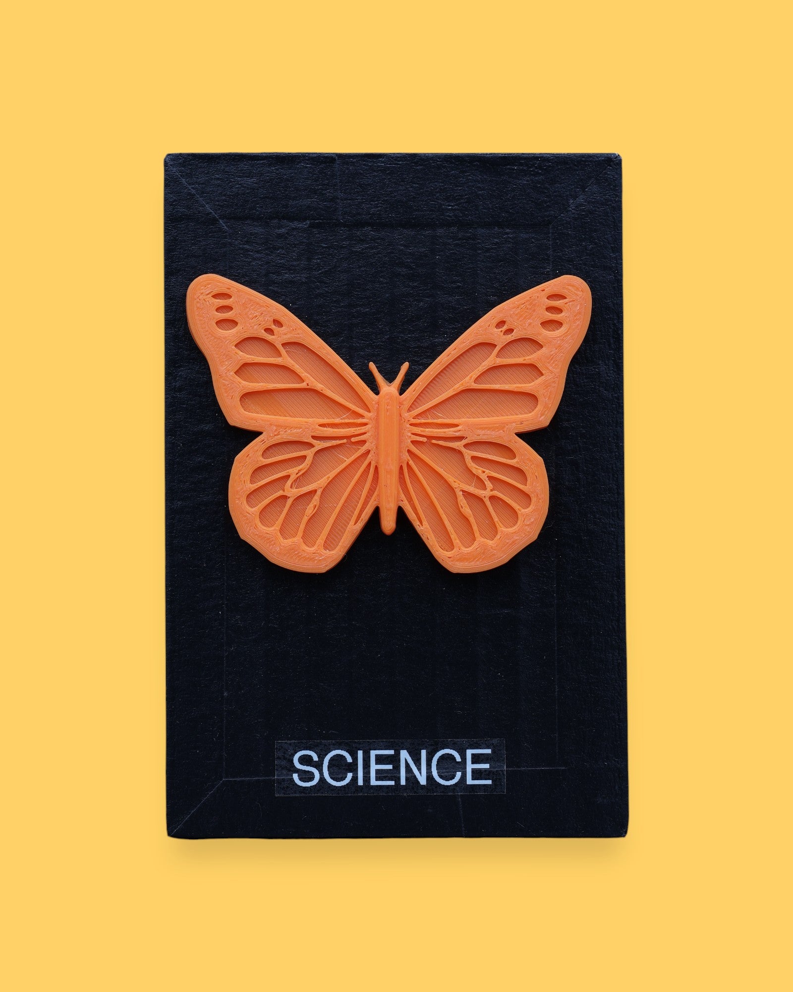 The Science symbol has a circular black magnet with a blue string attached to the magnet for security embedded in the center. Labeled "Science" in black font and white backing. The background of the symbol is white. 