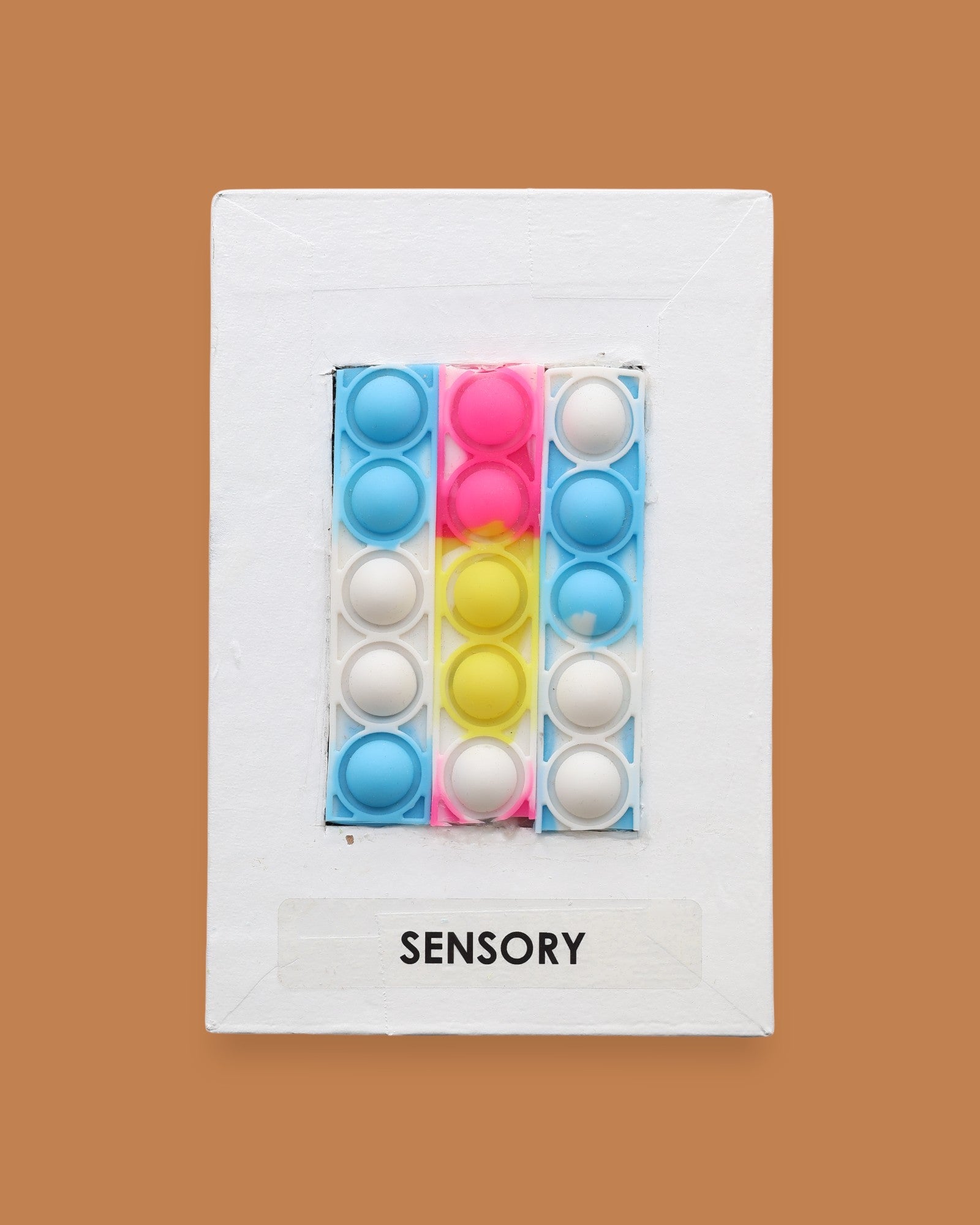 The Sensory Pop Fidget symbol with a multicolored pop-it style silicone fidget strip featuring the colors blue, pink, yellow, and white raised bubbles. Labeled "Sensory" in black font on white backing at the bottom of the symbol. The background of the symbol is white. 