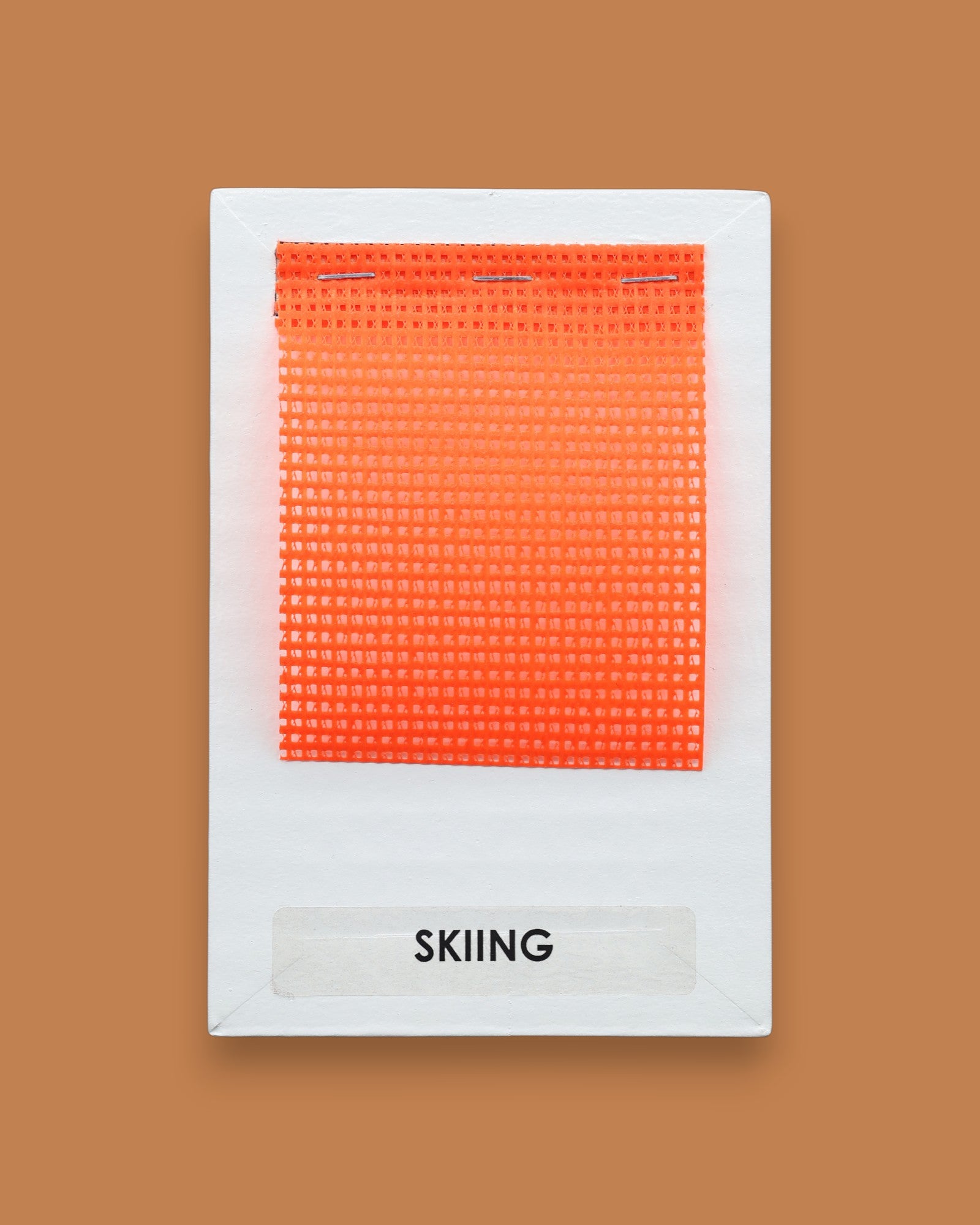 The Skiing symbol has a squared flourescent orange mesh fabric embedded in the center. Labeled "Skiing" in black font on white backing. The background of the symbol is white. 