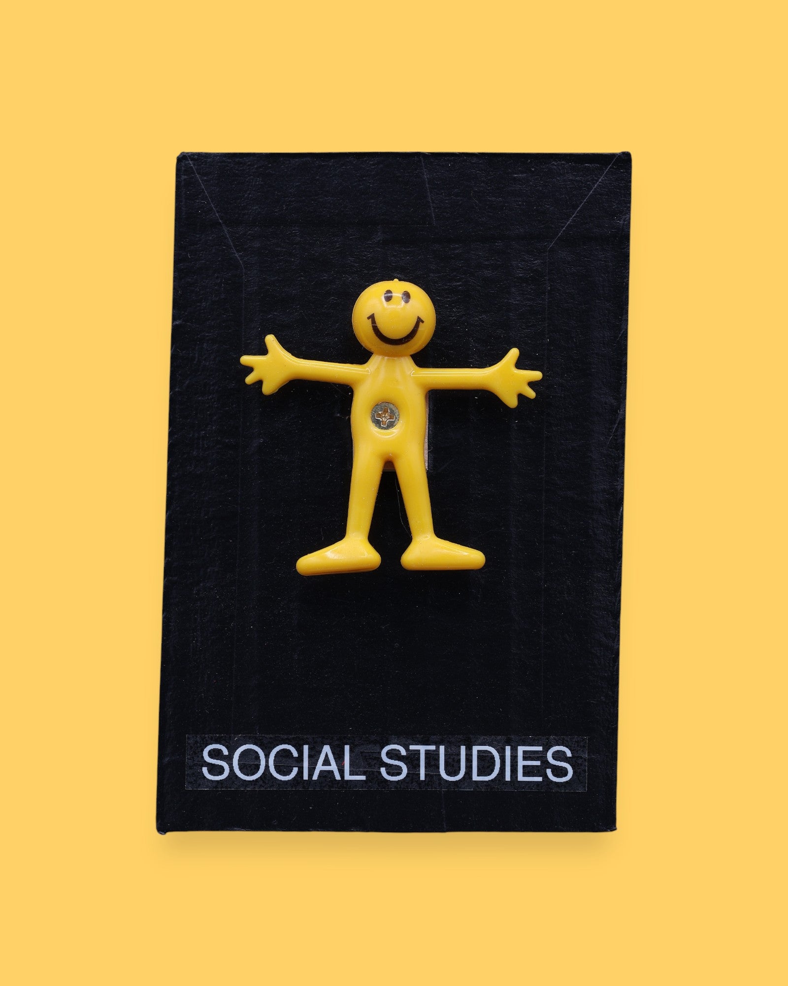 The Social Studies high constrast symbol with a yellow bendy figure embedded in the center. Labeled "Social Studies" in white font at the bottom of symbol on clear backing. The background of the symbol is black. 