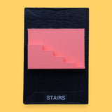 The Stairs symbol has a side profile of 3D printed stairs in bright coral orange PLA 3D printer filament. Labeled "Stairs" with black font on white backing at the bottom of symbol. The background of the symbol is white. 