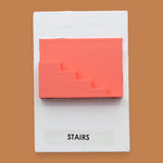 The Stairs symbol has a side profile of 3D printed stairs in bright coral orange PLA 3D printer filament. Labeled "Stairs" with black font on white backing at the bottom of symbol. The background of the symbol is white. 