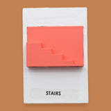 The Stairs symbol has a side profile of 3D printed stairs in bright coral orange PLA 3D printer filament. Labeled "Stairs" with black font on white backing at the bottom of symbol. The background of the symbol is white. 