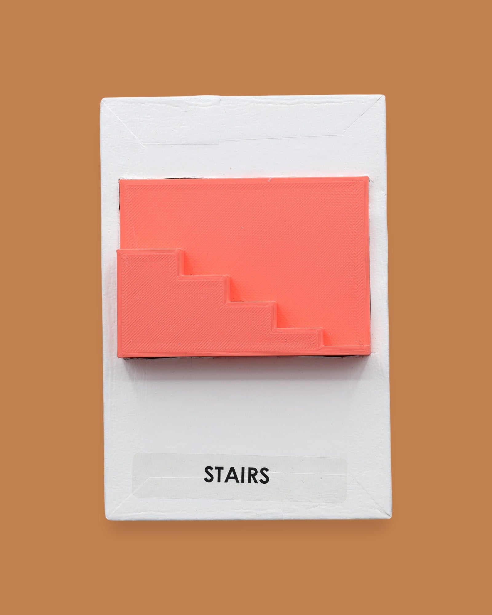The Stairs symbol has a side profile of 3D printed stairs in bright coral orange PLA 3D printer filament. Labeled "Stairs" with black font on white backing at the bottom of symbol. The background of the symbol is white. 