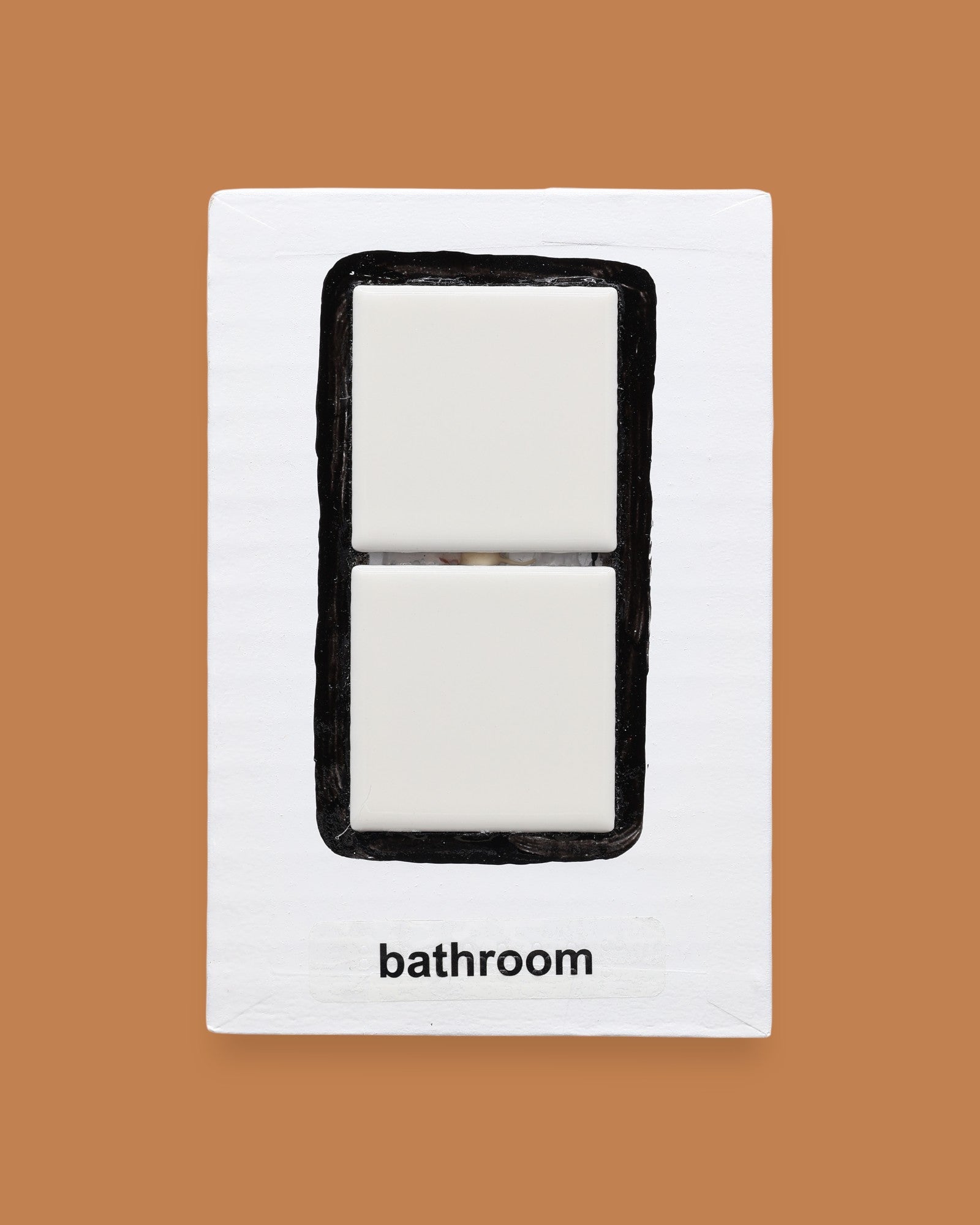 The Bathroom symbol has two square, white, ceramic tiles are embedded vertically in the center of the card with a black outline painted around the tiles. Labeled "Bathroom" in black font on white backing at the bottom the symobl. The background of the symbol is white.