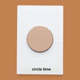 The Circle Time symbol with a tan wood-like 3D printed plastic circle embedded in the center. Labeled "Circle Time" in black font at the bottom of symbol on white backing. 