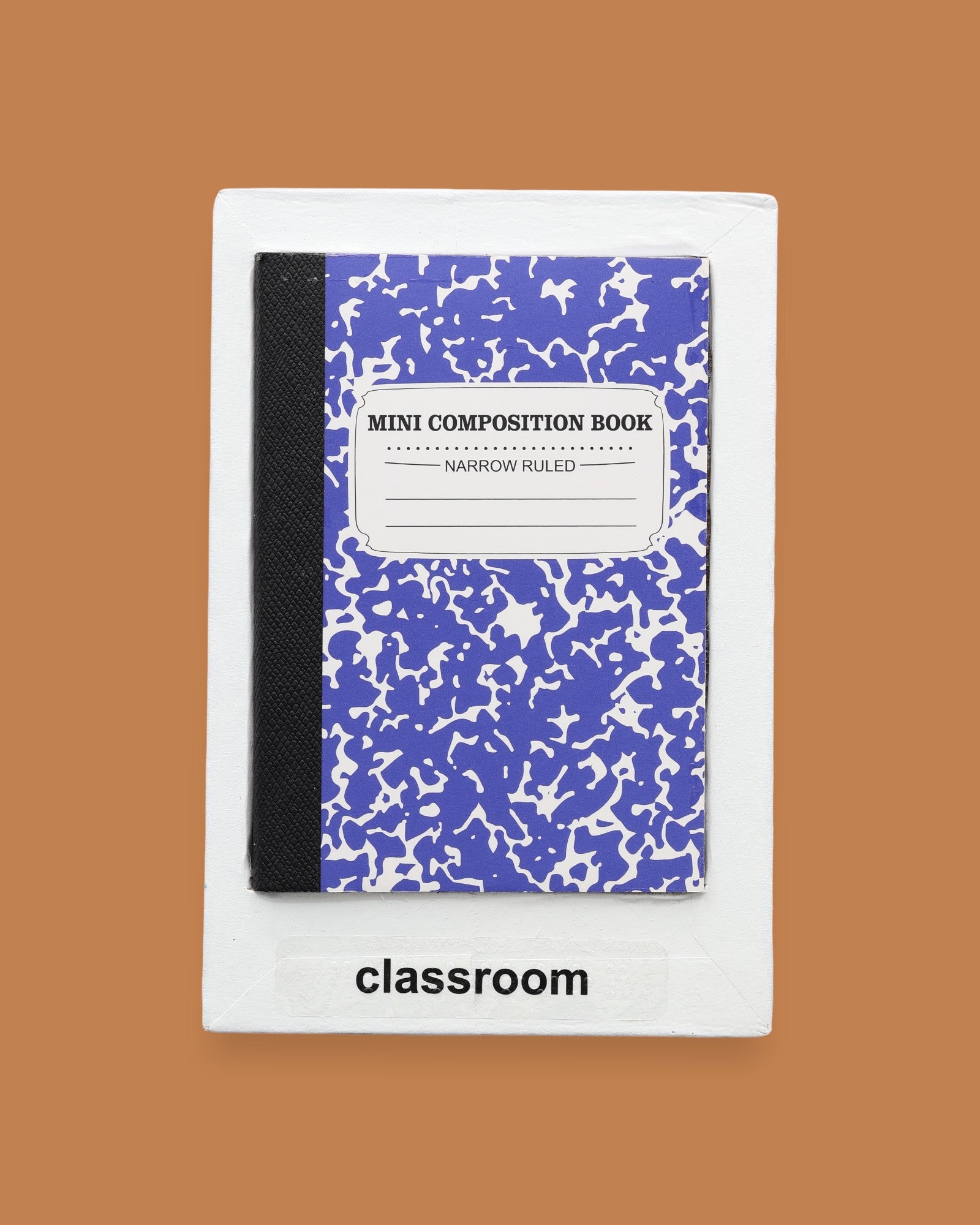 The Classroom symbol has a miniature  small marble composition notebook embedded in the center. Labeled "Classroom" in black font on white backing. The background of the symbol is white. 