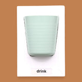 The Drink symbol has a light green cup with horizontal ridges embedded. Labeled "Drink" in white font and black backing at the bottom of symbol. The background of the symbol is white.