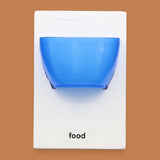 The Food symbol with a small plastic yellow bowl embedded in the center, color of bowl may vary. Labeled "Food" in black font at the bottom of symbol on white backing. 