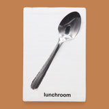 The Lunchroom symbol has a metal spoon embedded in the center. Labeled "Lunchroom" in black font on white backing at the bottom of symbol. The background of the symbol is white.