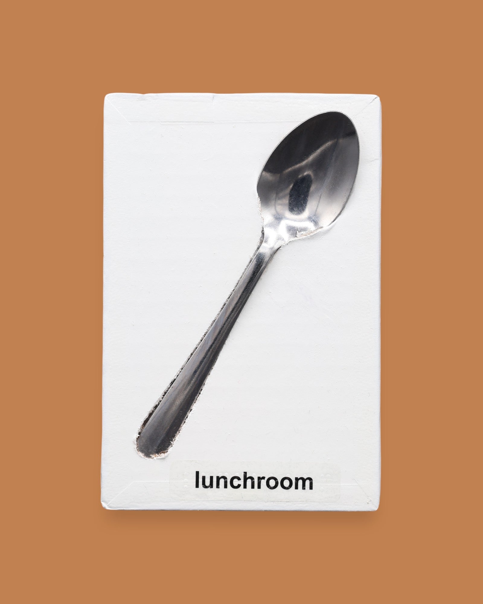 The Lunchroom symbol has a metal spoon embedded in the center. Labeled "Lunchroom" in black font on white backing at the bottom of symbol. The background of the symbol is white.