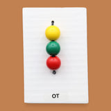 The OT symbol with colorful yellow, red, green beads on a cord attached vertically in the center. Labeled "OT" in black font at the bottom of symbol on white backing. The background of the symbol is white.