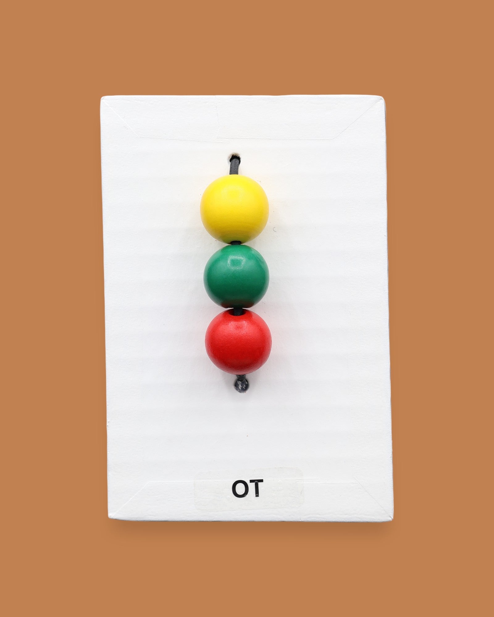 The OT symbol with colorful yellow, red, green beads on a cord attached vertically in the center. Labeled "OT" in black font at the bottom of symbol on white backing. The background of the symbol is white.