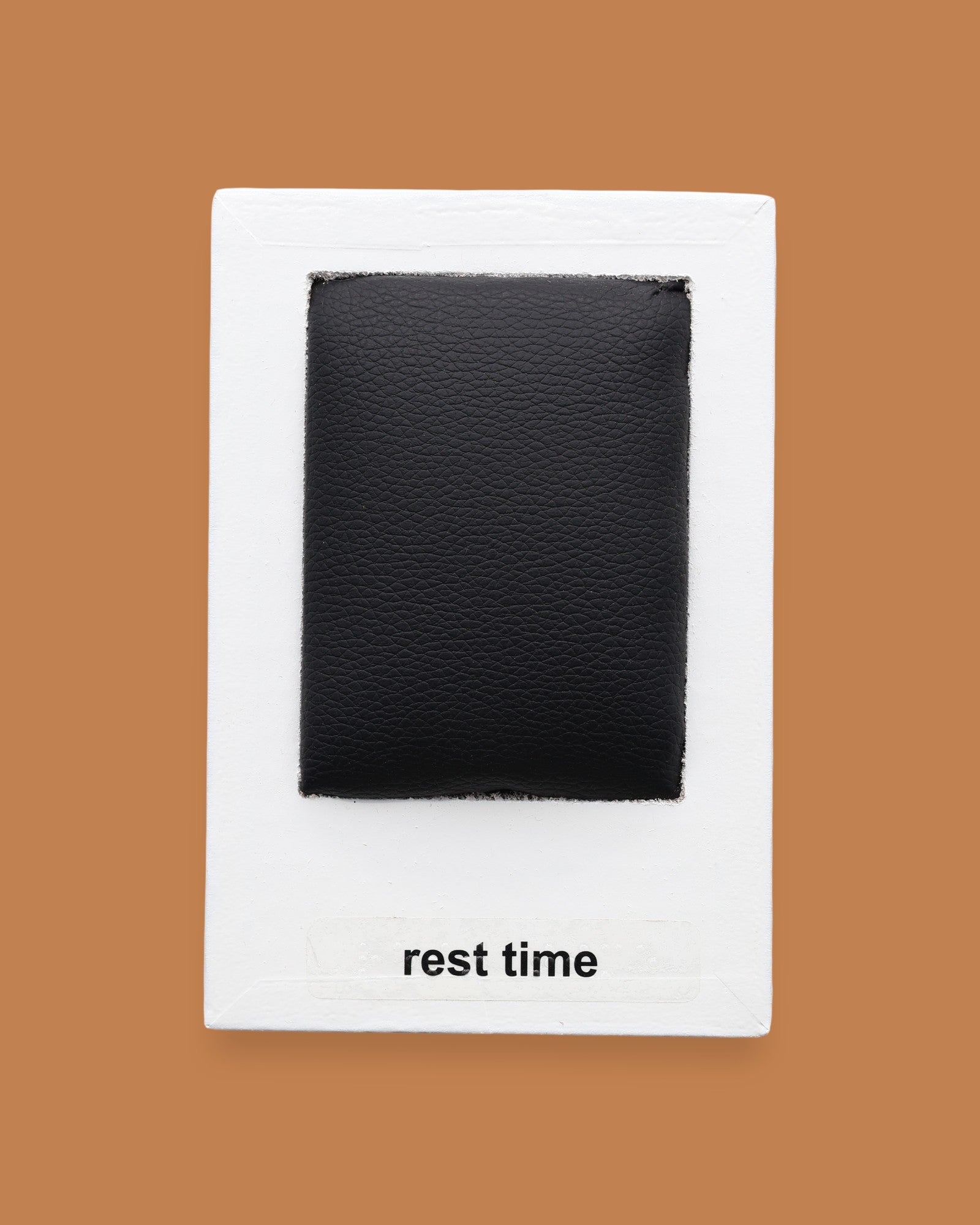The Rest Time symbol  with a piece of black mat like material embedded in the center. Labeled "Rest Time" in black font on white backing. The background of the symbol is white. 