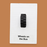The Wheels on the Bus symbol consists of a black toy-like wheel embedded in the center. Labeled "Wheels on the Bus" in black font on white backing at the bottom of symbol. The background of the symbol is white. 