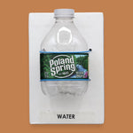 The image displays a standard white tactile card that is 4 by 6 inches in size with a small plastic Poland Springs water bottle attached to the card with blue string wrapped around it, the tactile card is labeled Water.