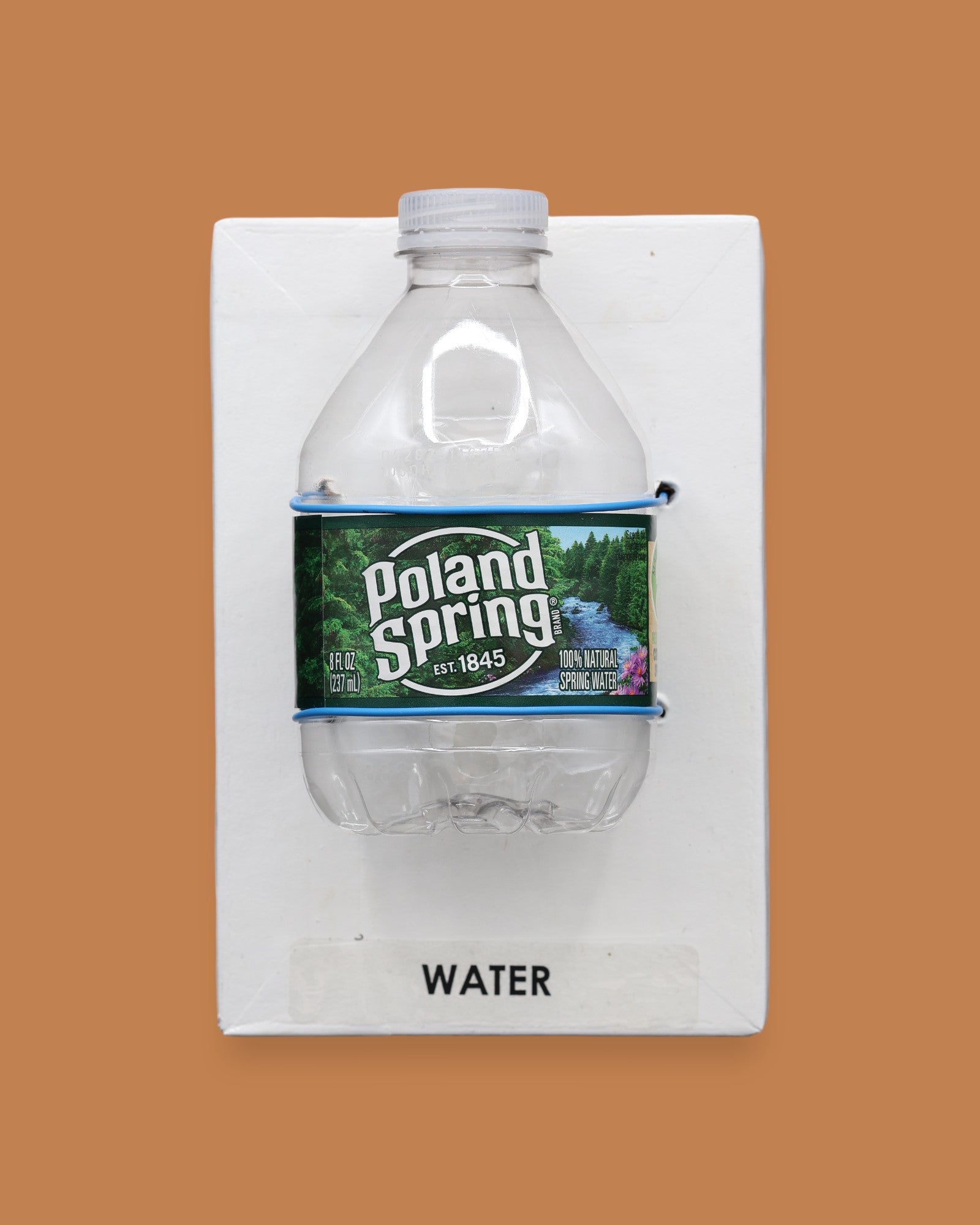 The image displays a standard white tactile card that is 4 by 6 inches in size with a small plastic Poland Springs water bottle attached to the card with blue string wrapped around it, the tactile card is labeled Water.