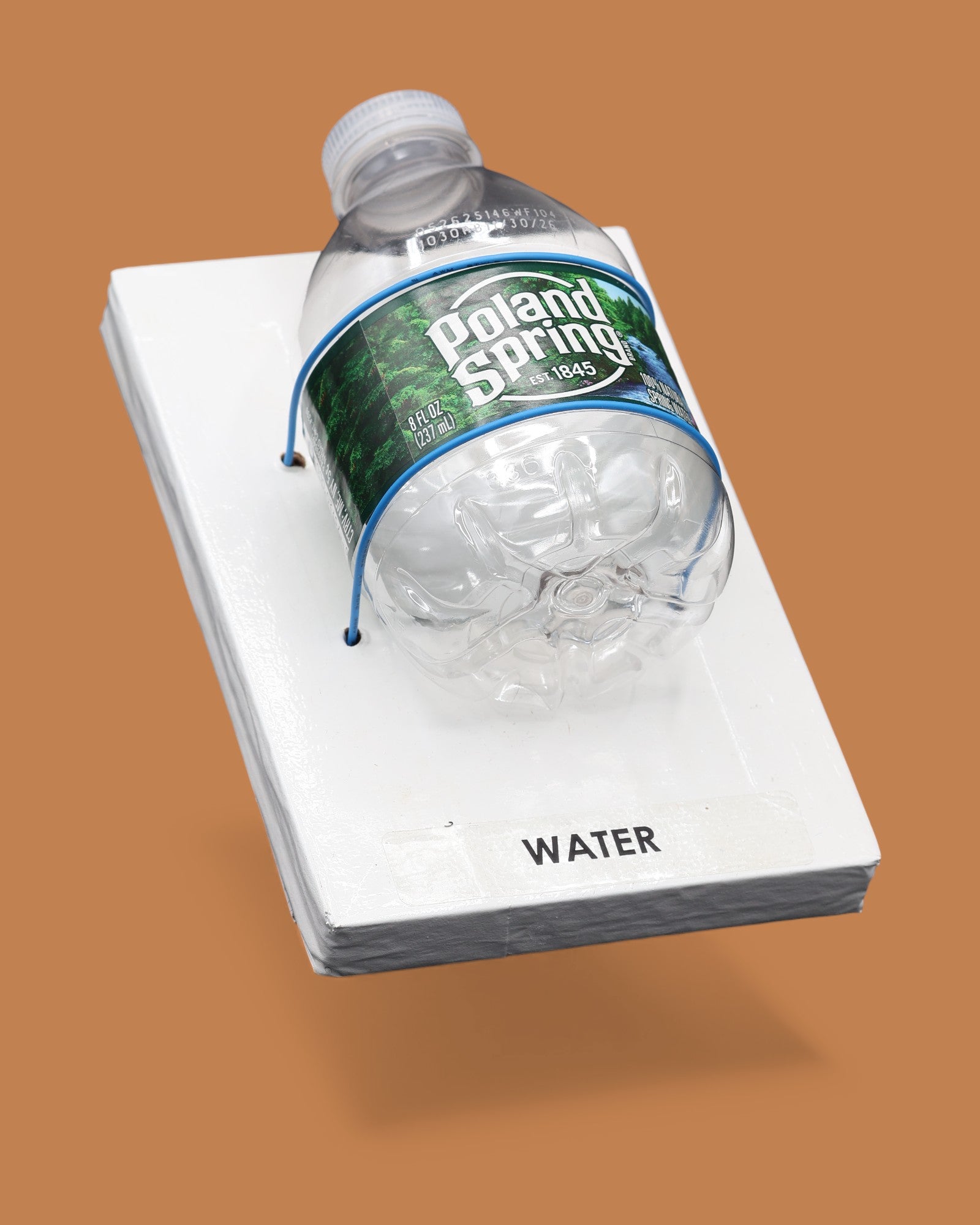 The image displays a white standard tactile card that is 4 by 6 inches in size with a small Poland Springs plastic water bottle attached to the card with blue string. The tactile card is labeled Water.