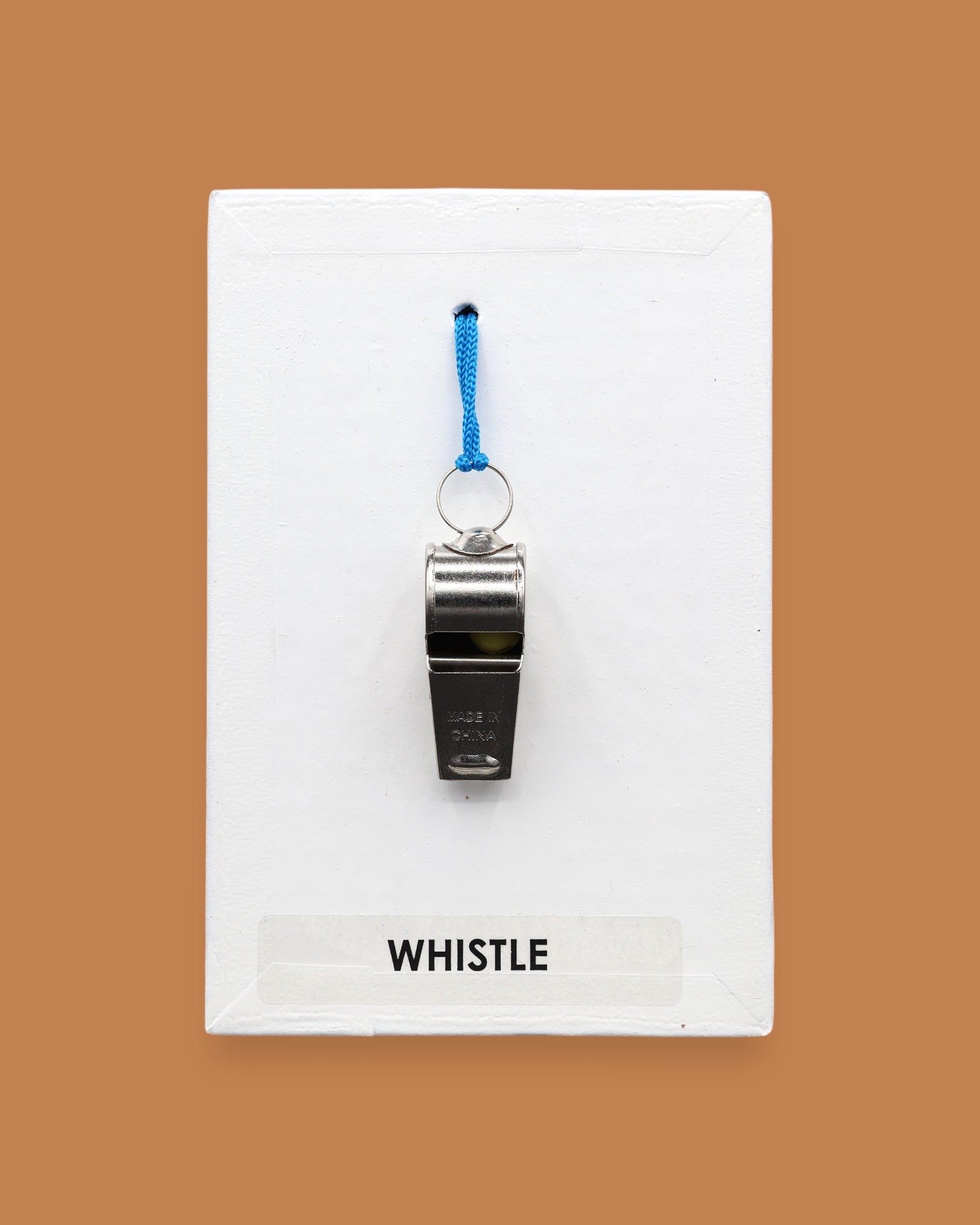 The Whistle symbol embedded with a sliver metal whistle attached with a blue cord embedded in the center of the card vertically. Labeled "Whistle" in black font on white backing at the bottom of the symbol. The background of the symbol is white. 
