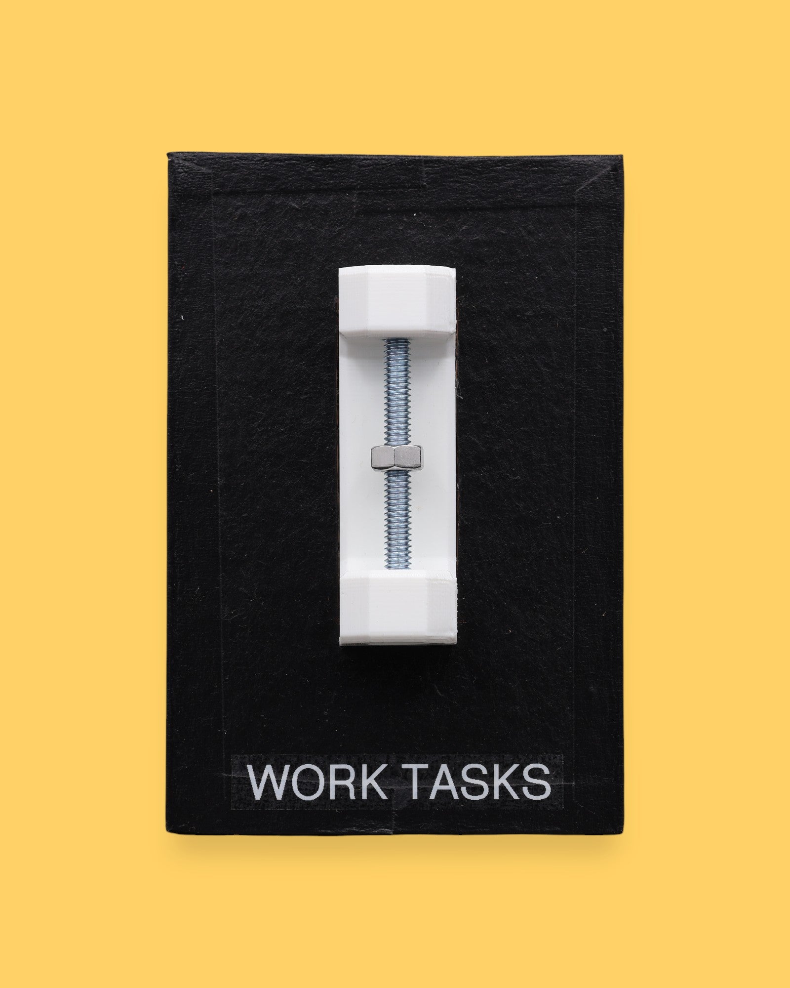 The Work Tasks symbol with an embedded bolt and nut assembly mounted on a black base vertically in the center. Labeled "Work Tasks" in white font on black backing at the bottom of the symbol. The background of the symbol is black. 