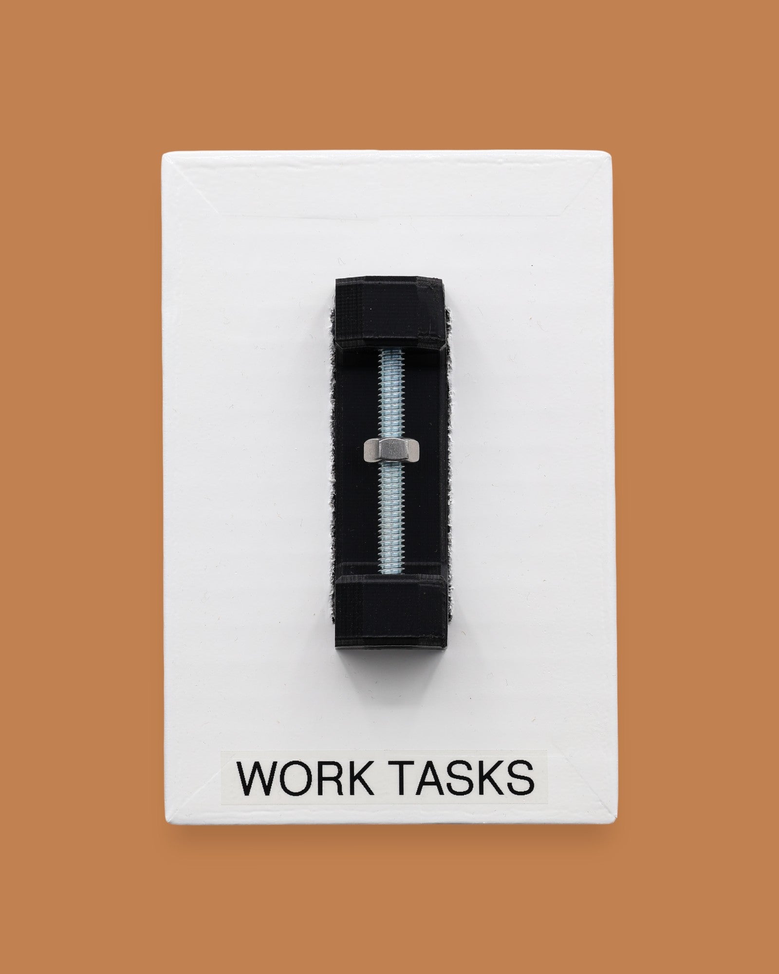 The Work Tasks symbol with an embedded bolt and nut assembly mounted on a black base vertically in the center. Labeled "Work Tasks" in black font on white backing at the bottom of the symbol. The background of the symbol is white. 